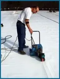 A man is using a machine on a white roof.
