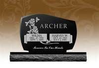 A black polished granite tombstone for Wilma and Harvey W. Archer, featuring floral carvings and a rustic stone base.