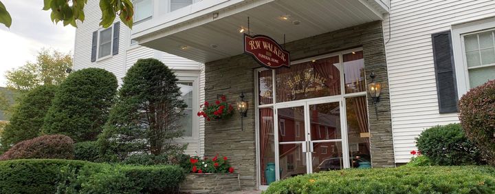 The entrance to La Scala restaurant features a stone facade, glass doors, and a hanging sign under a white covered porch.