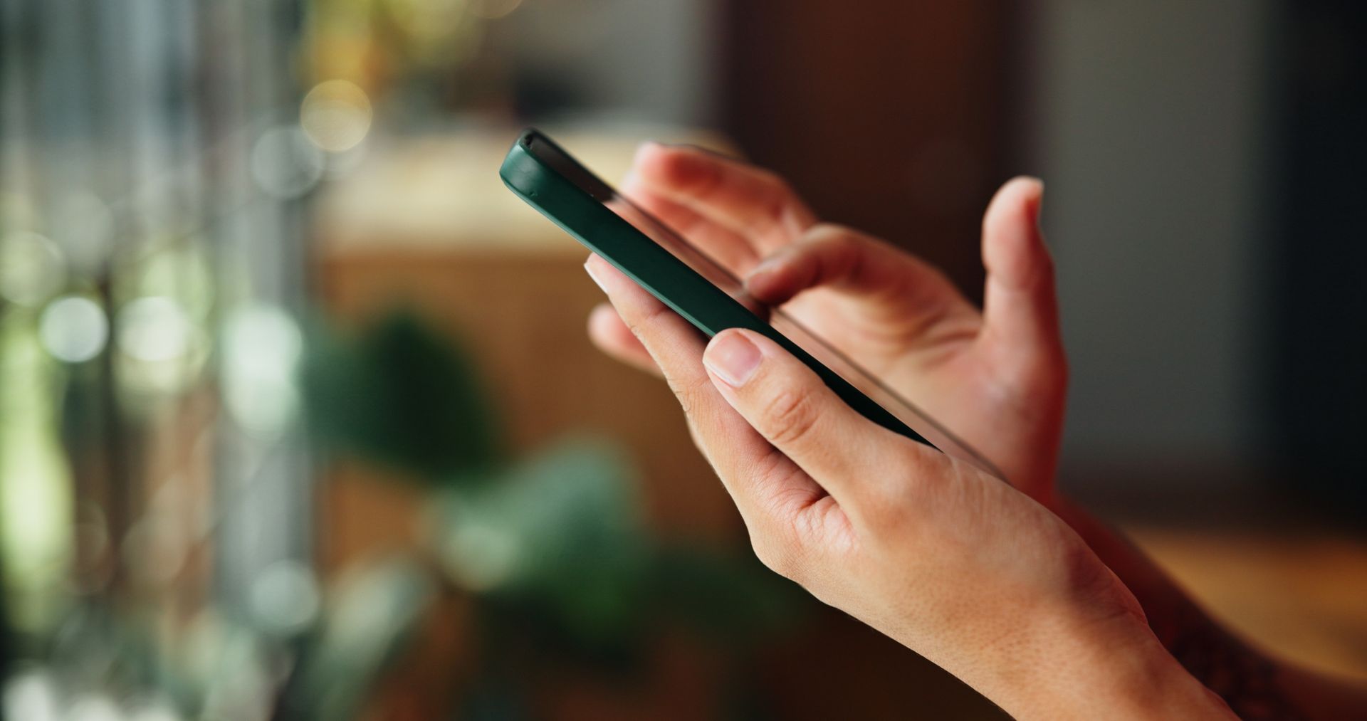 Close-up of hands holding a dark smartphone, with blurred indoor background.