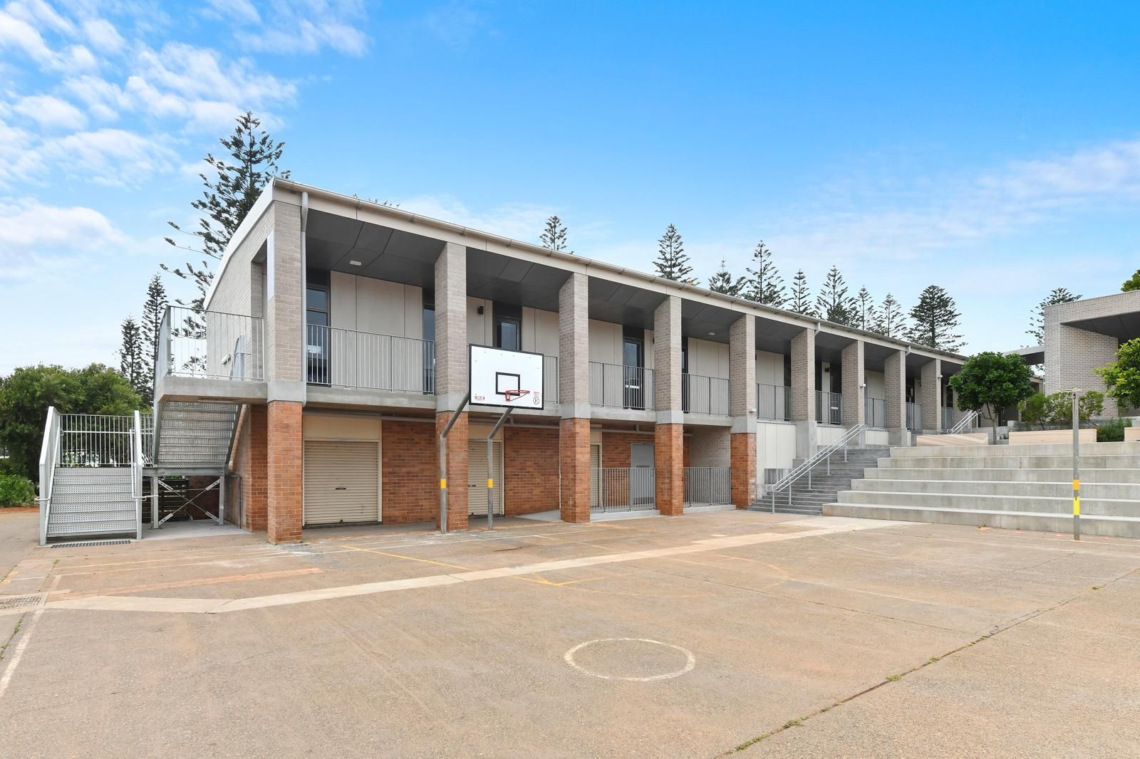 Outdoor school building with a basketball hoop and empty paved courtyard under a blue sky — Millers Masonry In Port Macquarie, NSW