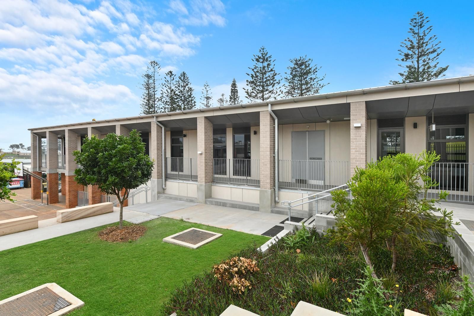 Modern apartment courtyard with white balconies, green lawn, and trees under a blue sky — Millers Masonry In Port Macquarie, NSW
