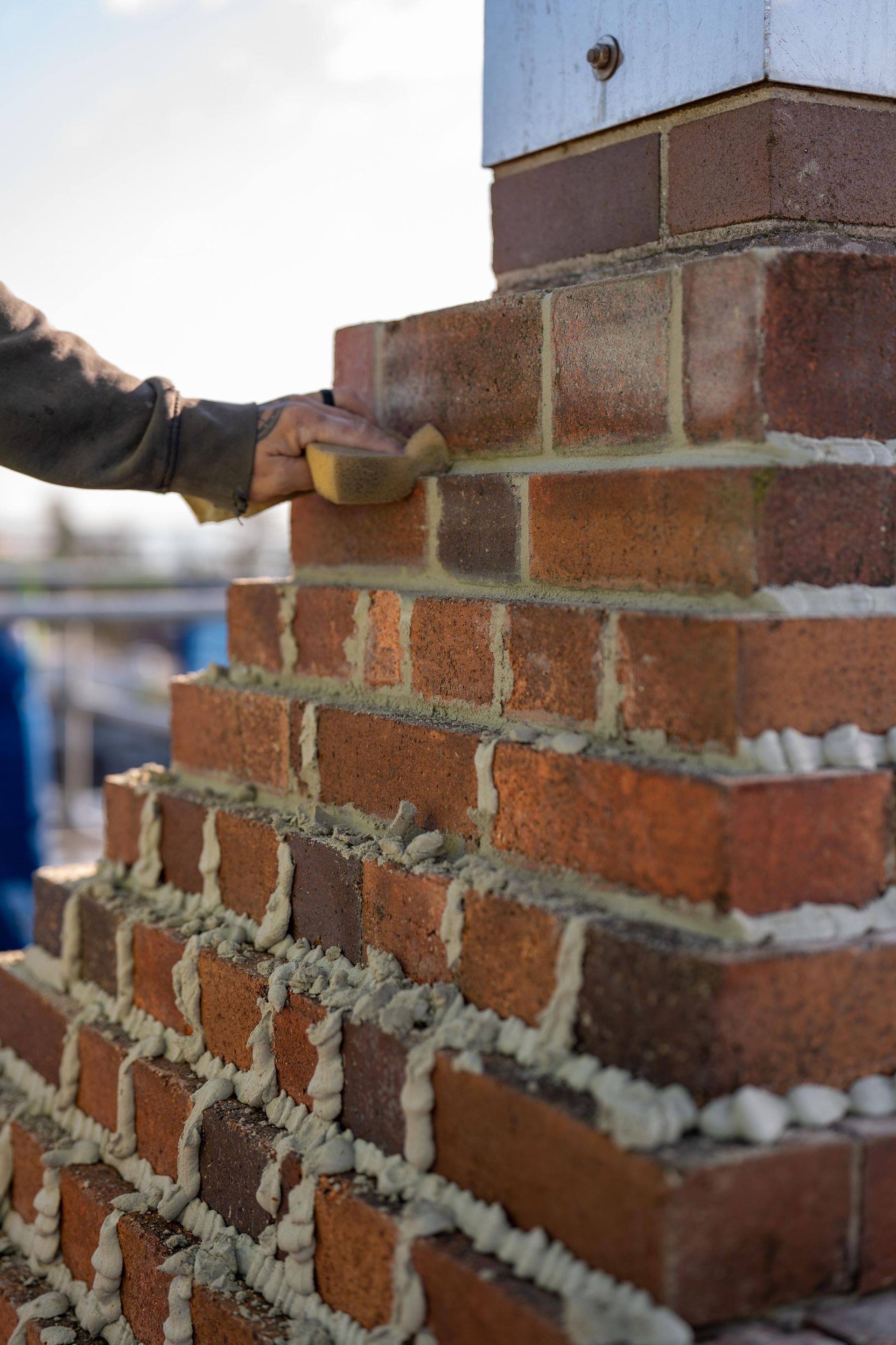 A Person's Hand Using a Sponge to Smooth Mortar on A Brick — Millers Masonry In Port Macquarie, NSW