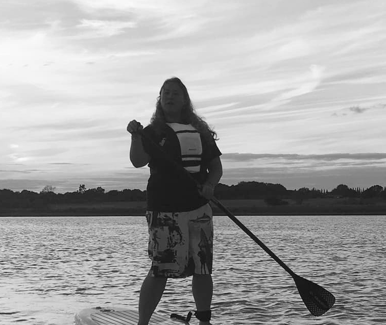 Person on a paddleboard on a lake, holding paddle. Sunset sky in background.
