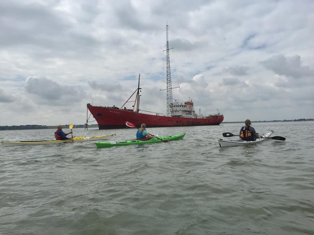 Kayakers on water near large red ship under cloudy sky.