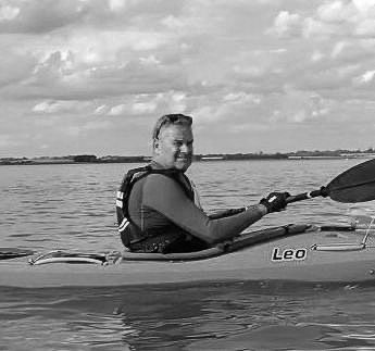 Man kayaking on calm water, holding paddle, wearing life vest, and smiling.