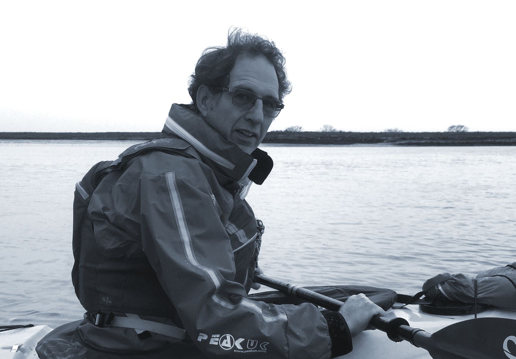 Man in kayak on water, wearing life vest, holding paddle, looking at camera.