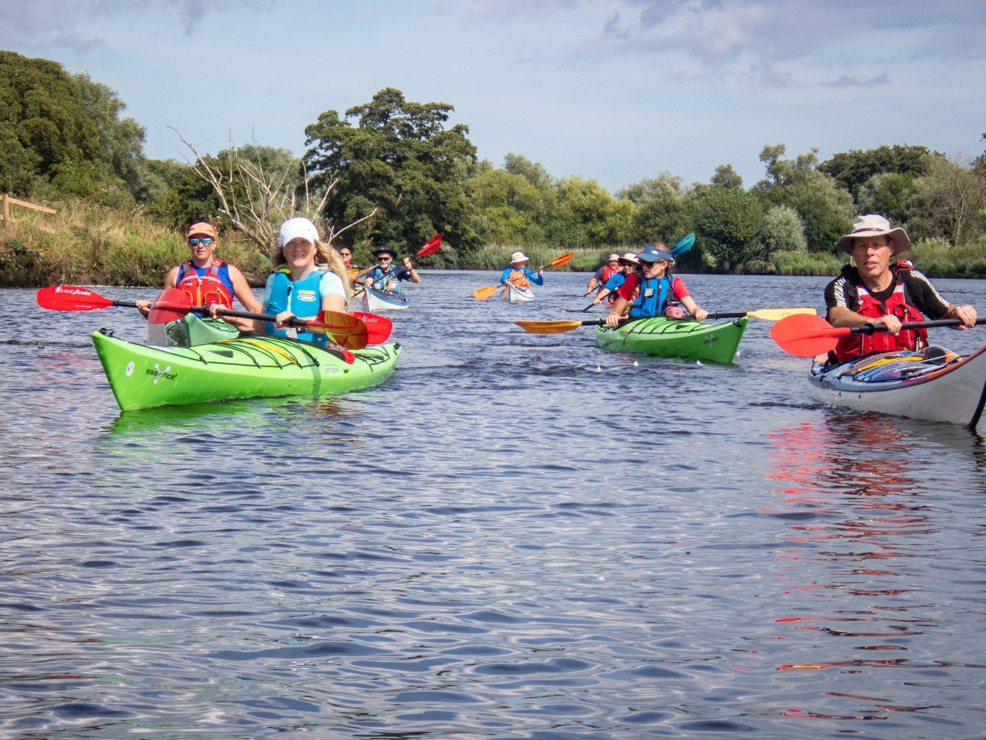 Kayakers paddling on a calm river on a sunny day. Green and white kayaks with colorful paddles.