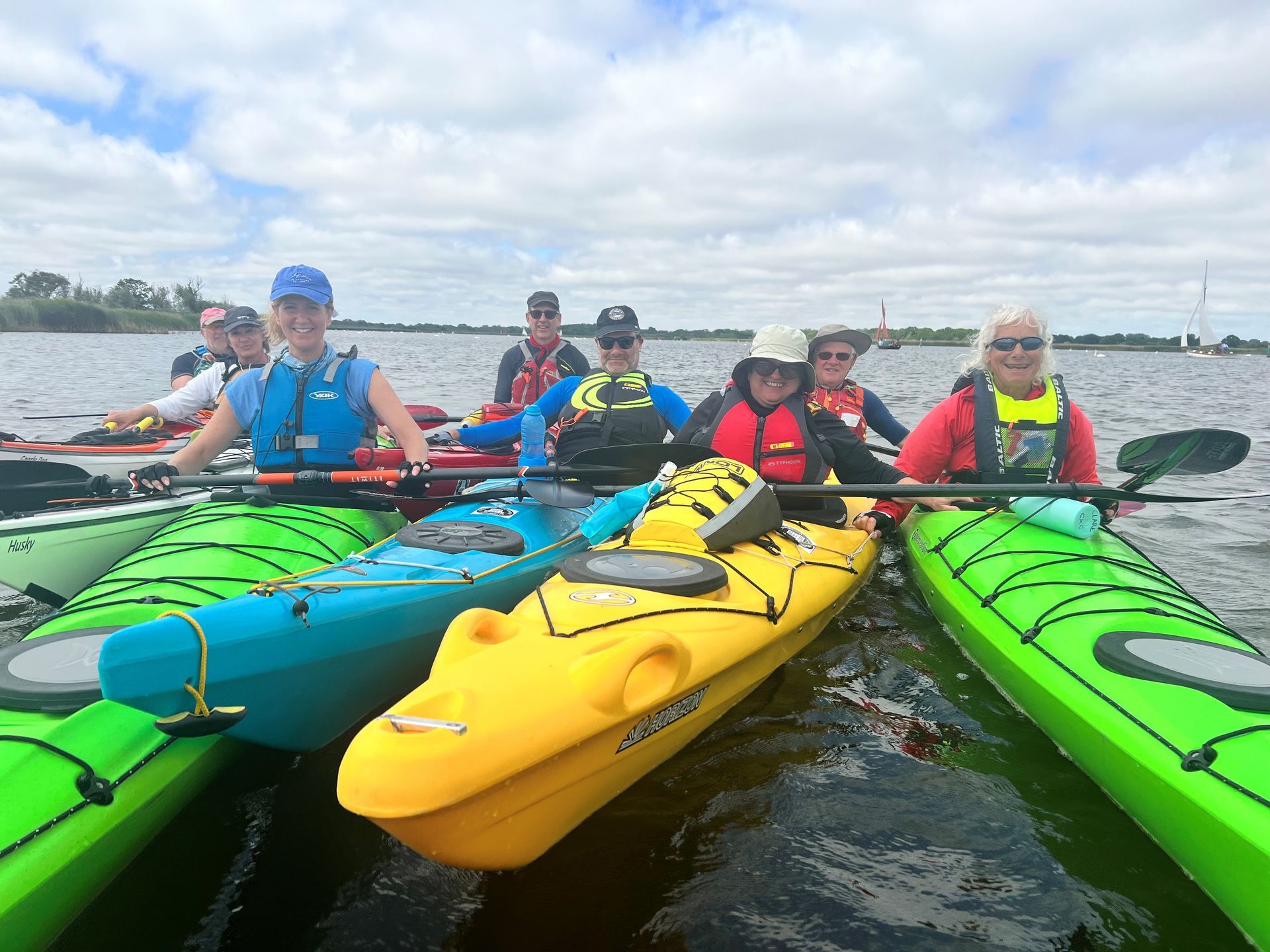 Group of kayakers on a lake. Several kayaks, brightly colored, with people smiling and holding paddles, overcast sky.