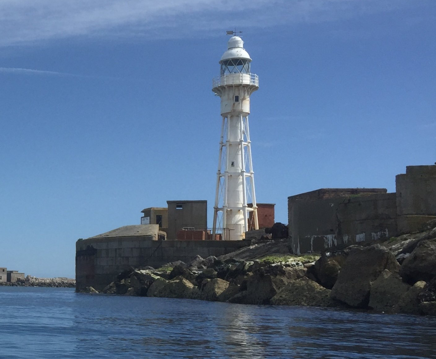 White lighthouse on a rocky coast under a clear blue sky.