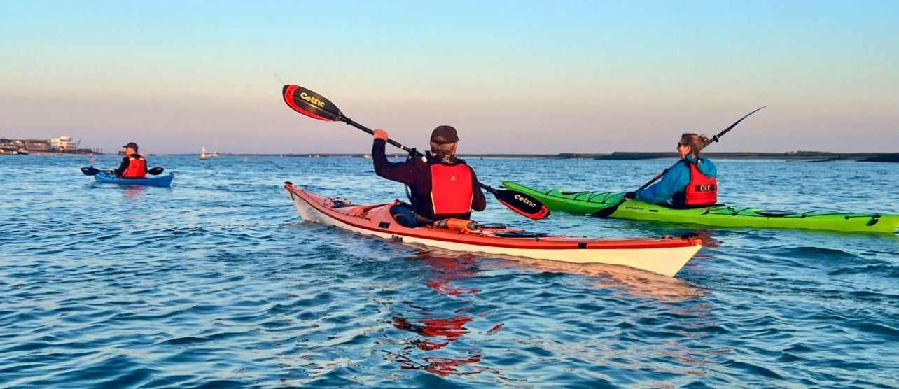 Three people kayaking on blue water; a coastal setting with clear skies.