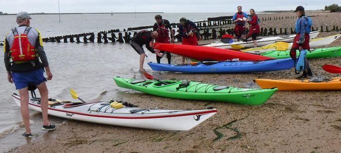 People preparing kayaks on a sandy beach. Kayaks are various colors.