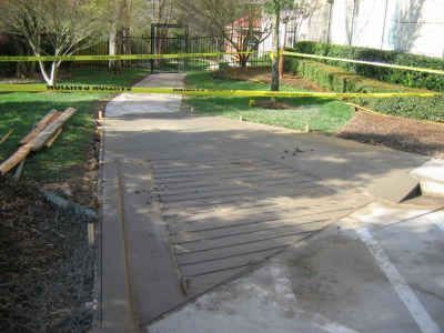 Newly poured concrete walkway with rebar, grass, and yellow caution tape surrounding the construction zone.