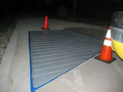 A large gray ramp with blue trim on a concrete surface at night, with two orange traffic cones and part of a yellow vehicle.