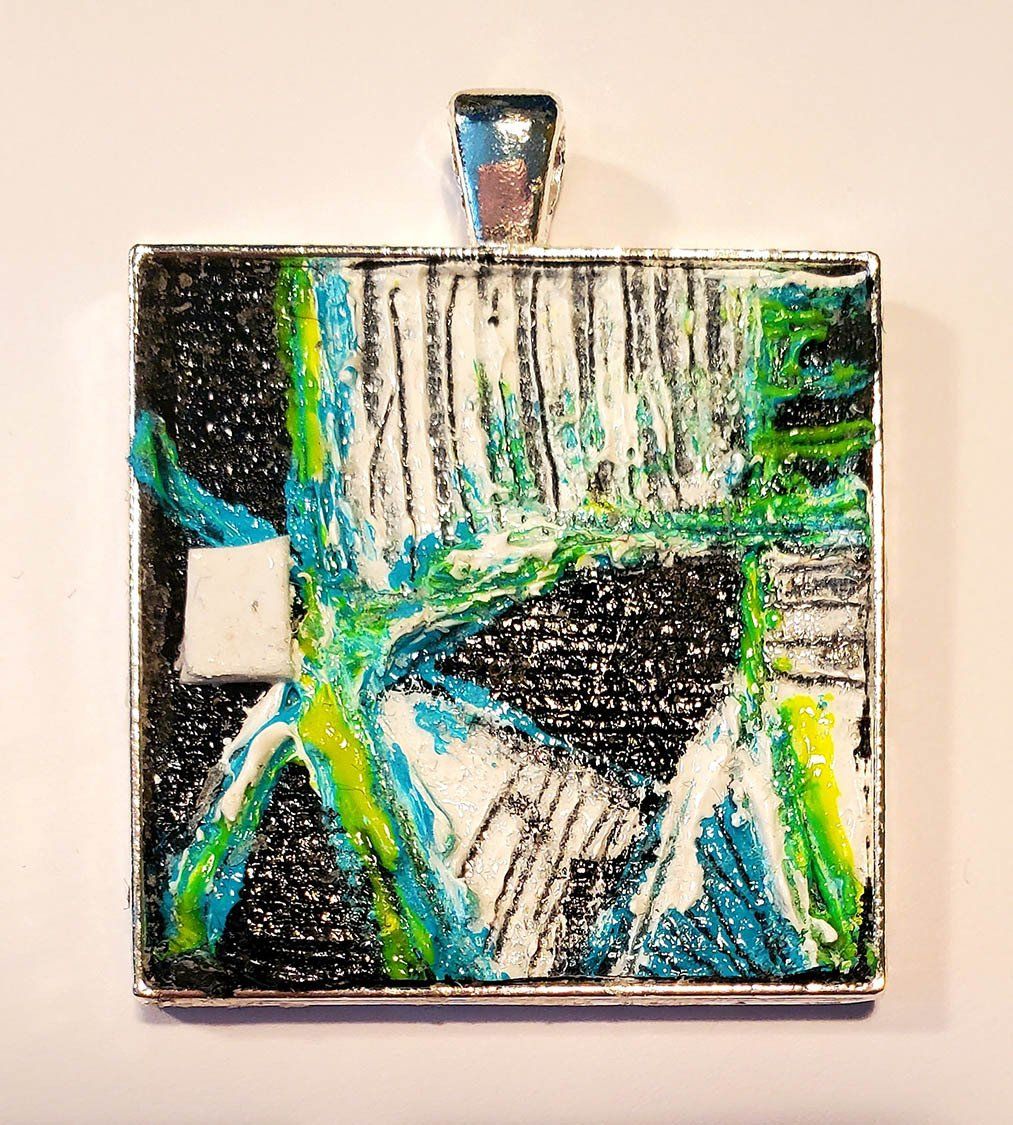 A square pendant with a painting on it is on a white surface.