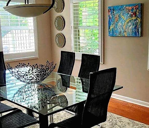 A dining room with a glass table and chairs and a painting on the wall.