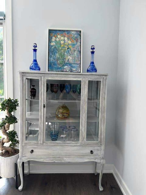 A white hutch with blue vases and a painting on top of it.