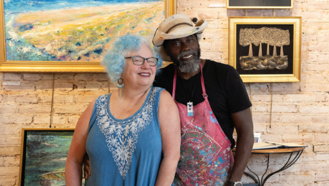 A man and a woman are posing for a picture in front of paintings.