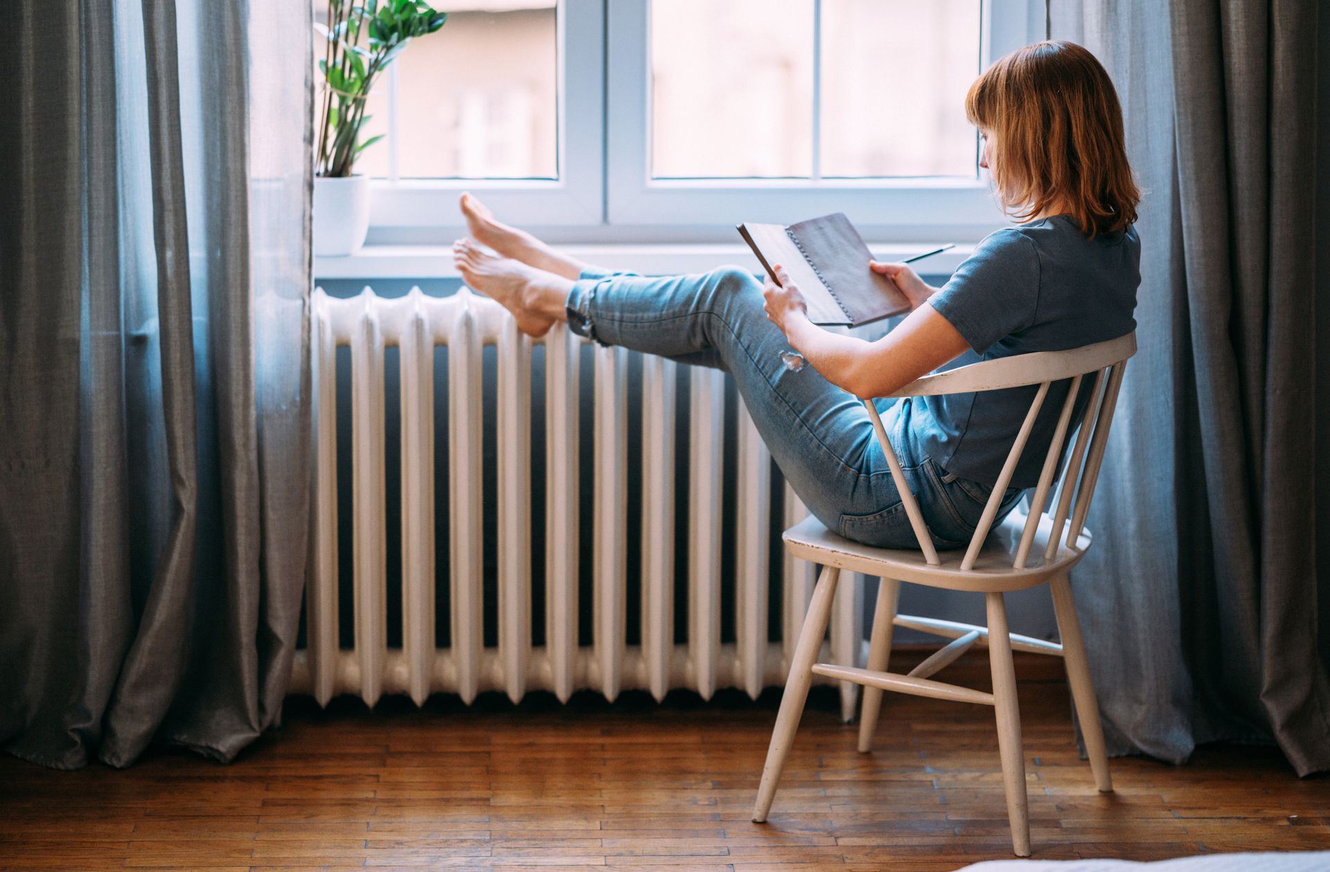 A Woman Is Sitting in a Chair in Front of a Radiator Reading a Book — Independence, MO — McIntosh Heating & Cooling