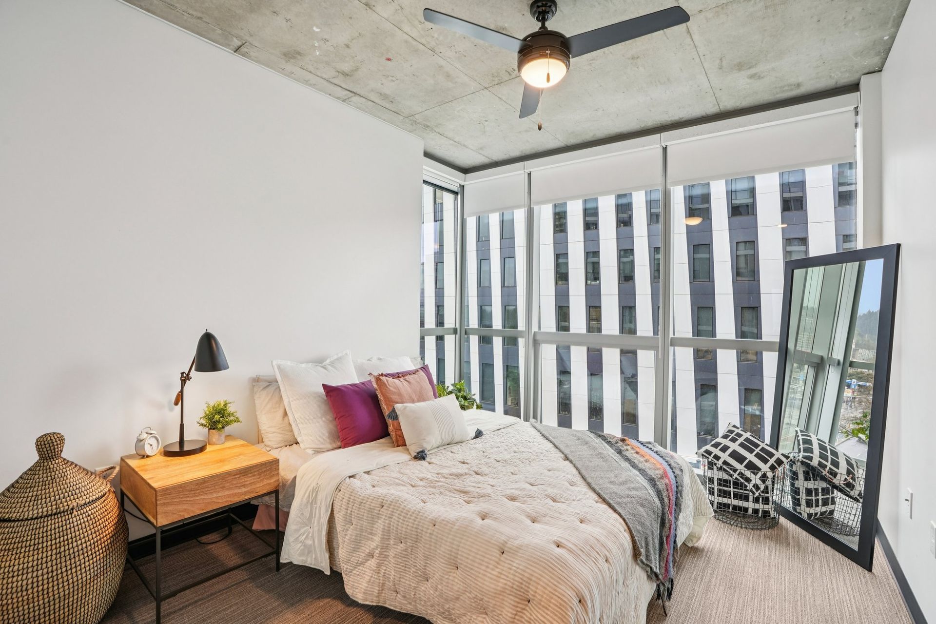 Collective on 4th apartment bedroom featuring large windows, exposed concrete ceilings, a mirror.