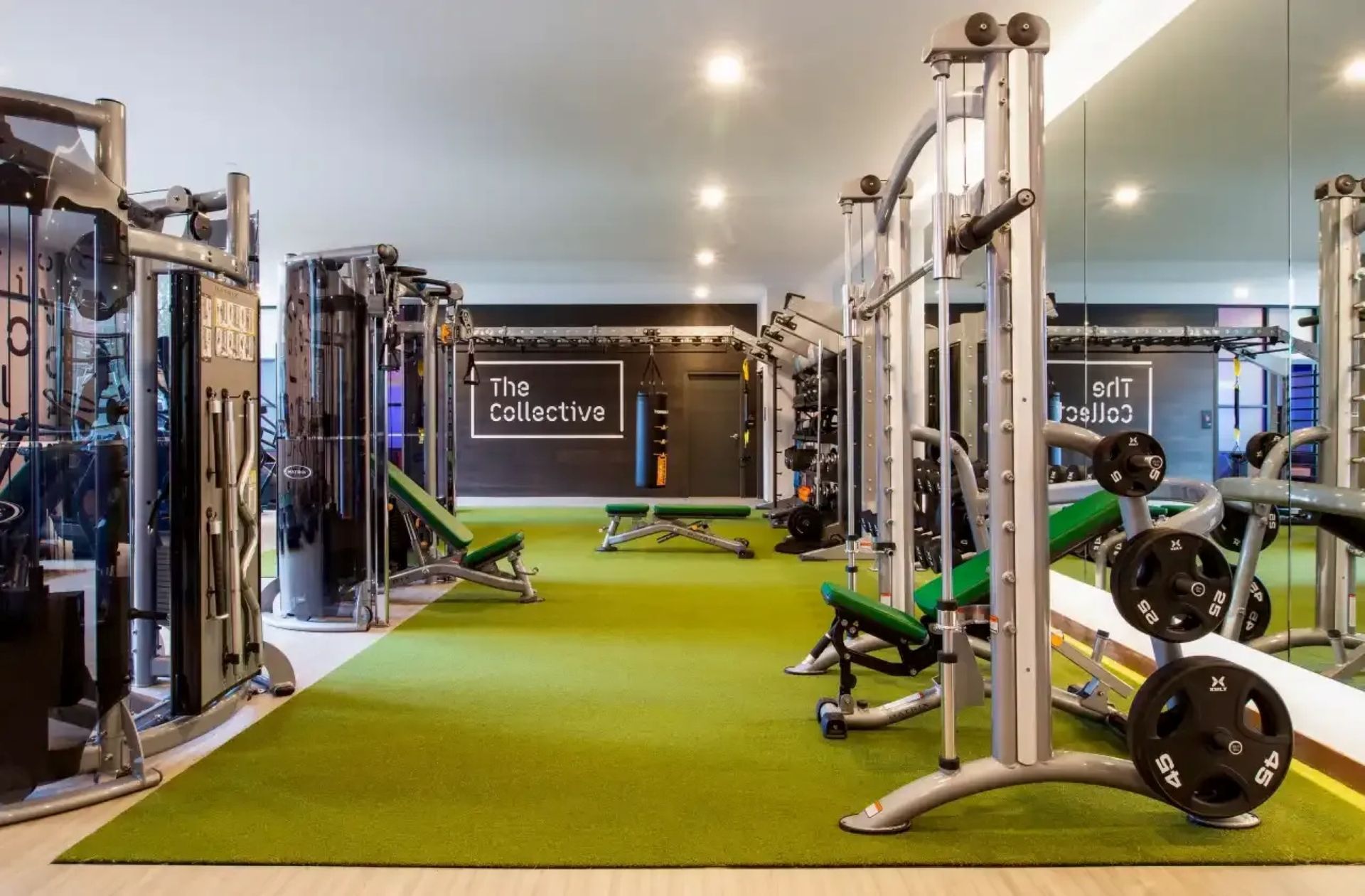 Modern gym interior with green turf, cable machines, weight benches, and mirrors