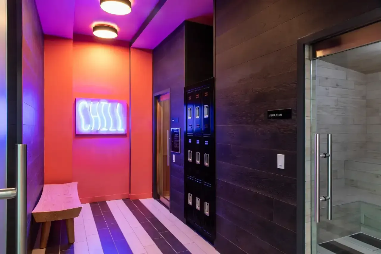 Colorful locker room with a neon CHILL sign, purple lighting, lockers, and a steam room door.