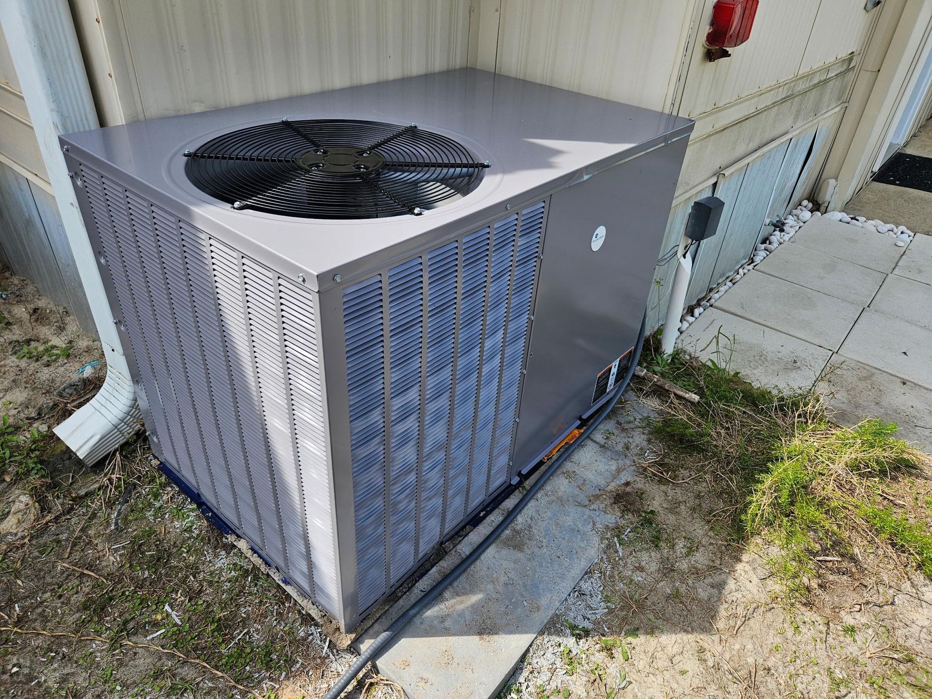 Outdoor central air conditioner unit beside a house wall on a concrete pad with grass nearby