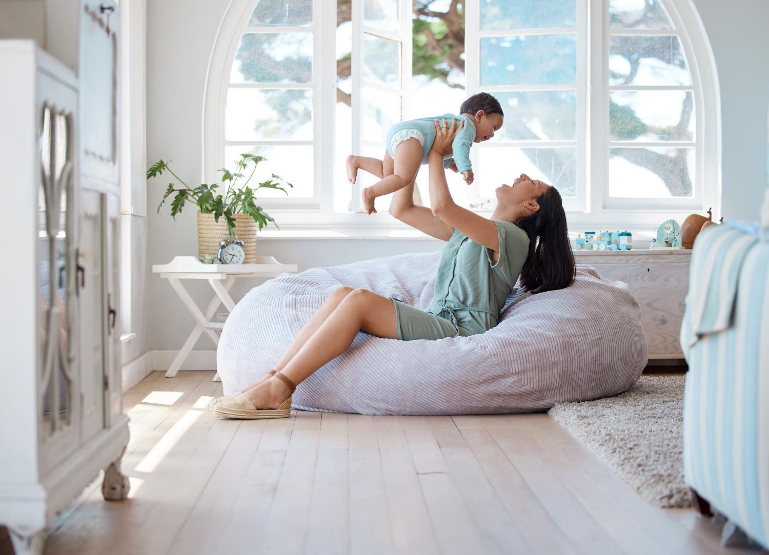 Woman lifting baby in a bright living room by a large arched window