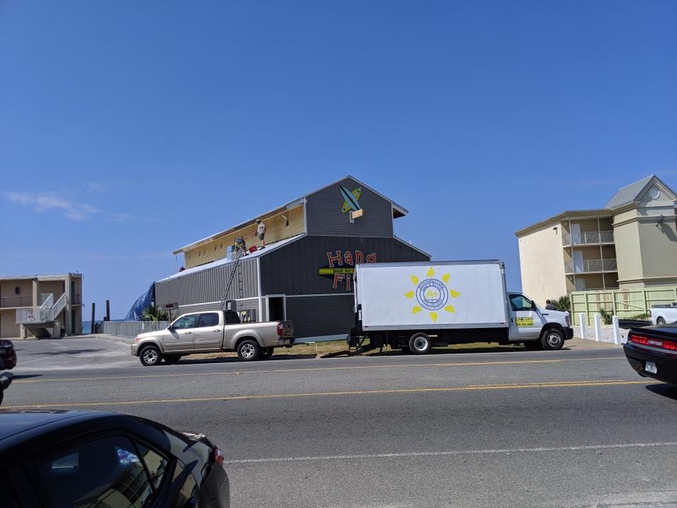 White box truck parked outside a dark building with a colorful sign on a sunny street.
