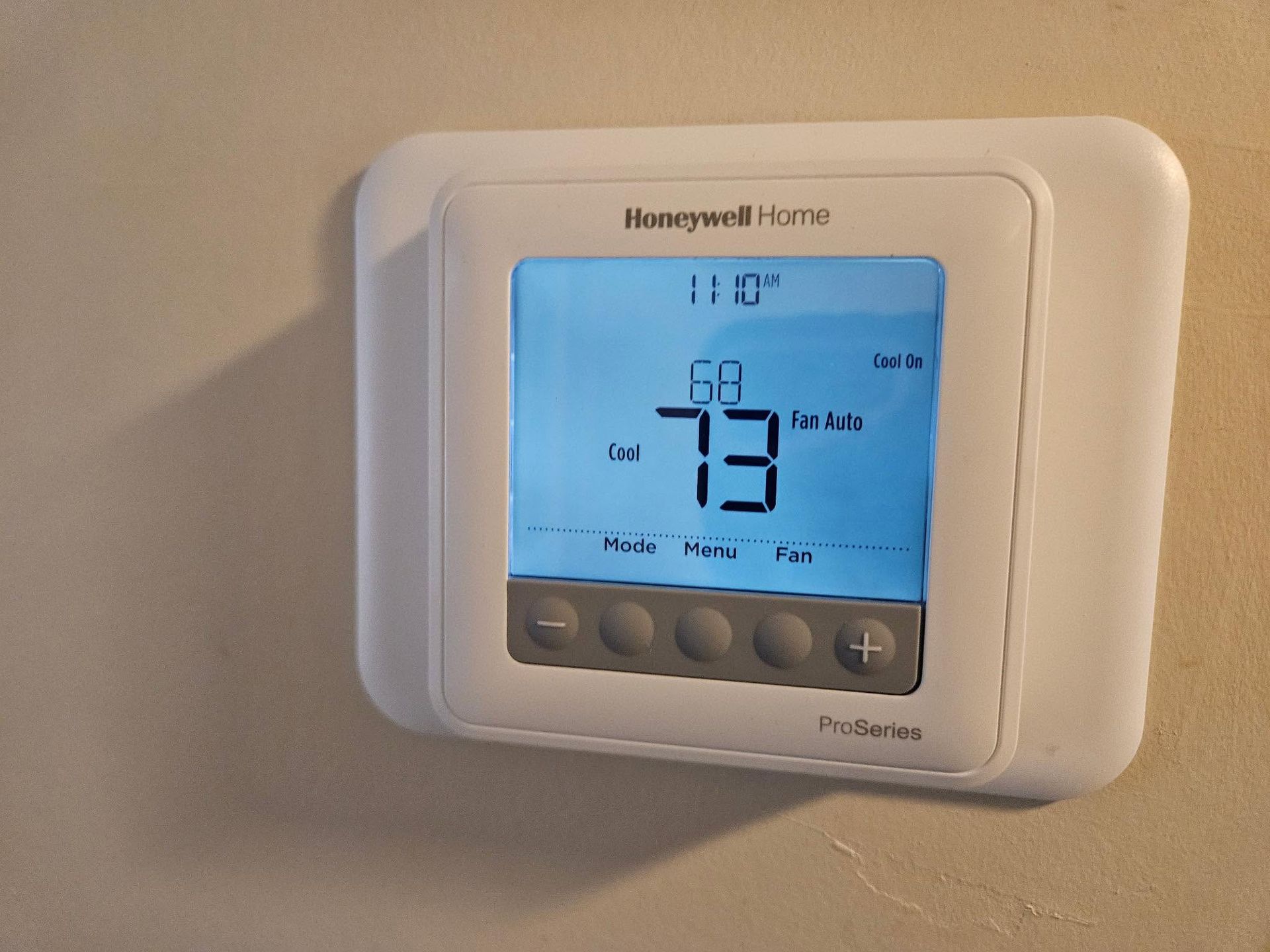 Honeywell Home thermostat on a wall, showing 73°F on a blue-lit digital display.