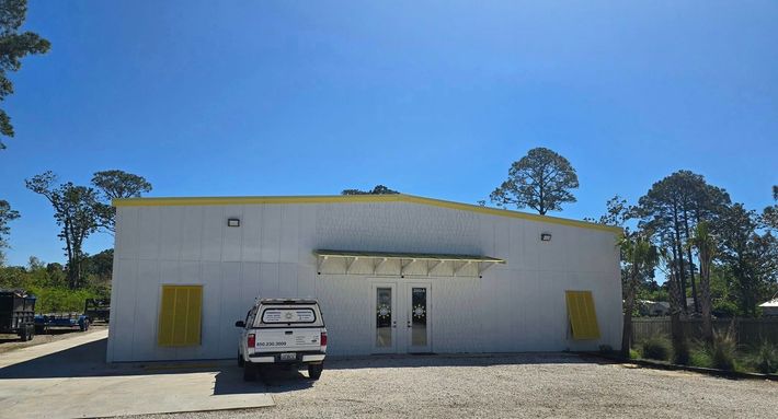 White industrial building with a central door, flanked by yellow shutters, and a white SUV parked in front.