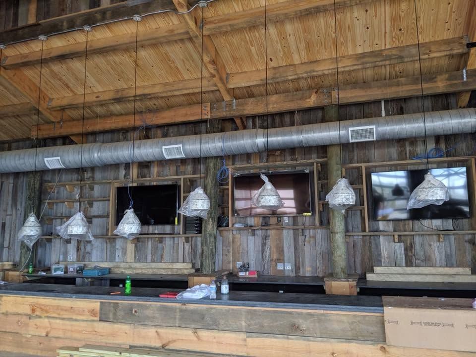 Rustic indoor bar with hanging silver pendant lights, wooden walls, and a long counter with stools.