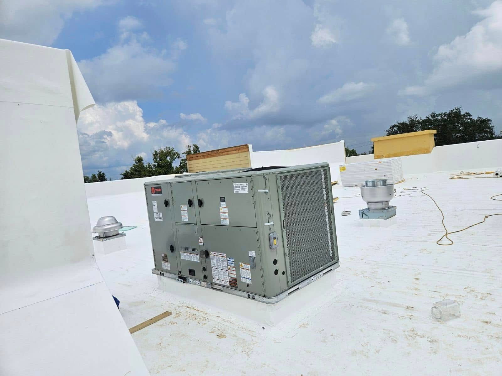 Gray HVAC unit on a white rooftop with vents, ducts, and cloudy sky in the background