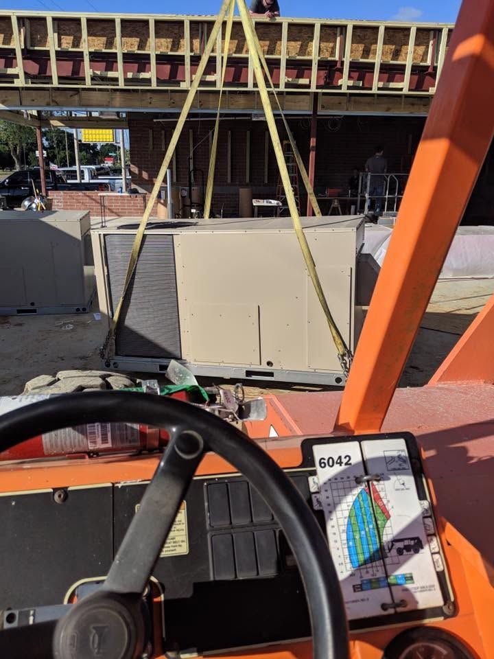 Construction site from a vehicle cab, with lifted HVAC unit on an orange forklift.