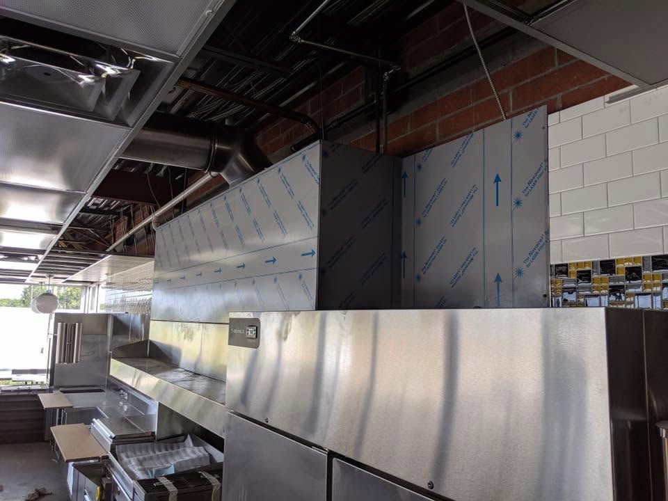 Industrial kitchen with stainless steel equipment and vents along a tiled wall