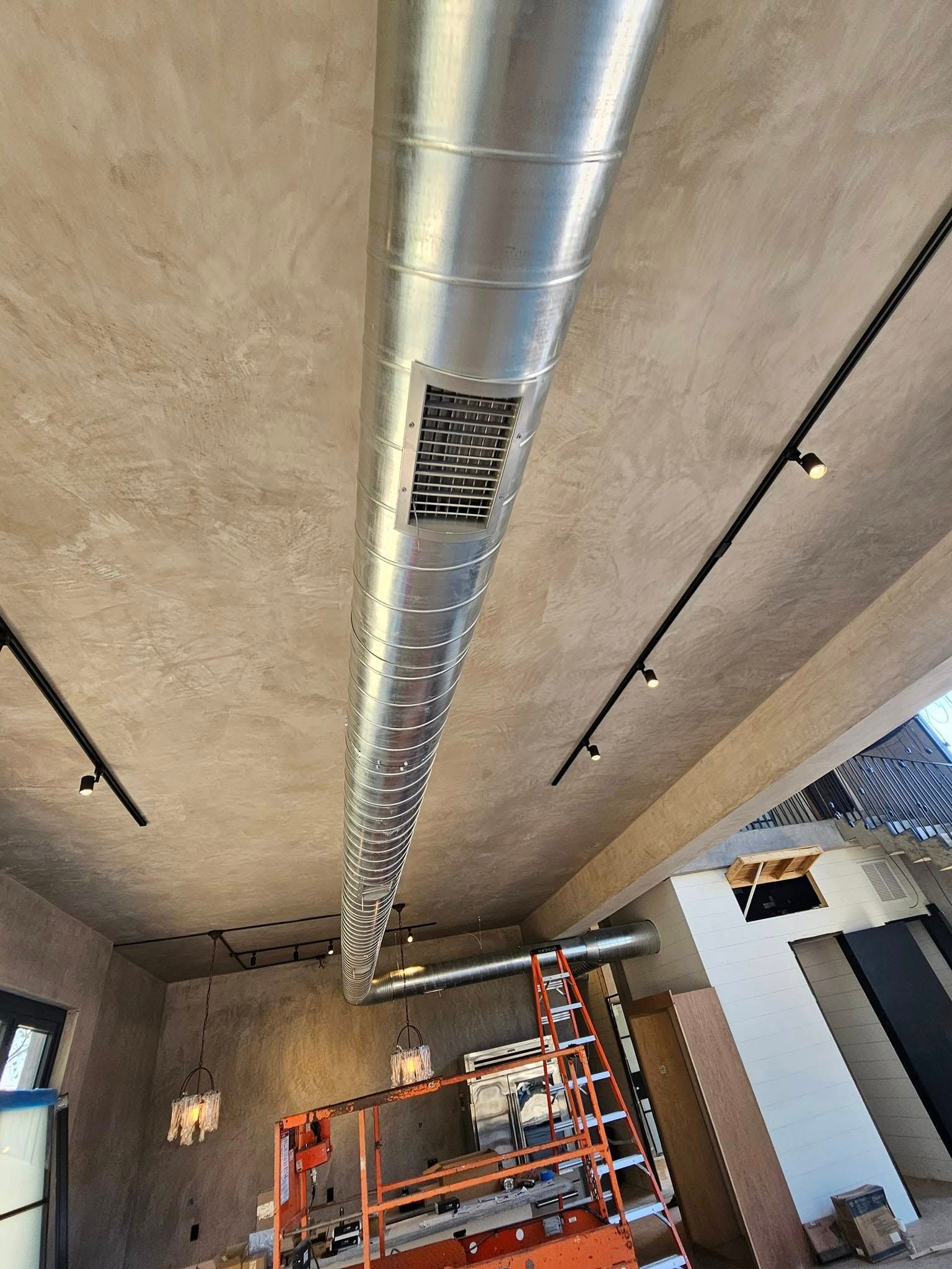 Interior ceiling with exposed HVAC ductwork, track lights, and orange scaffolding in a room under construction