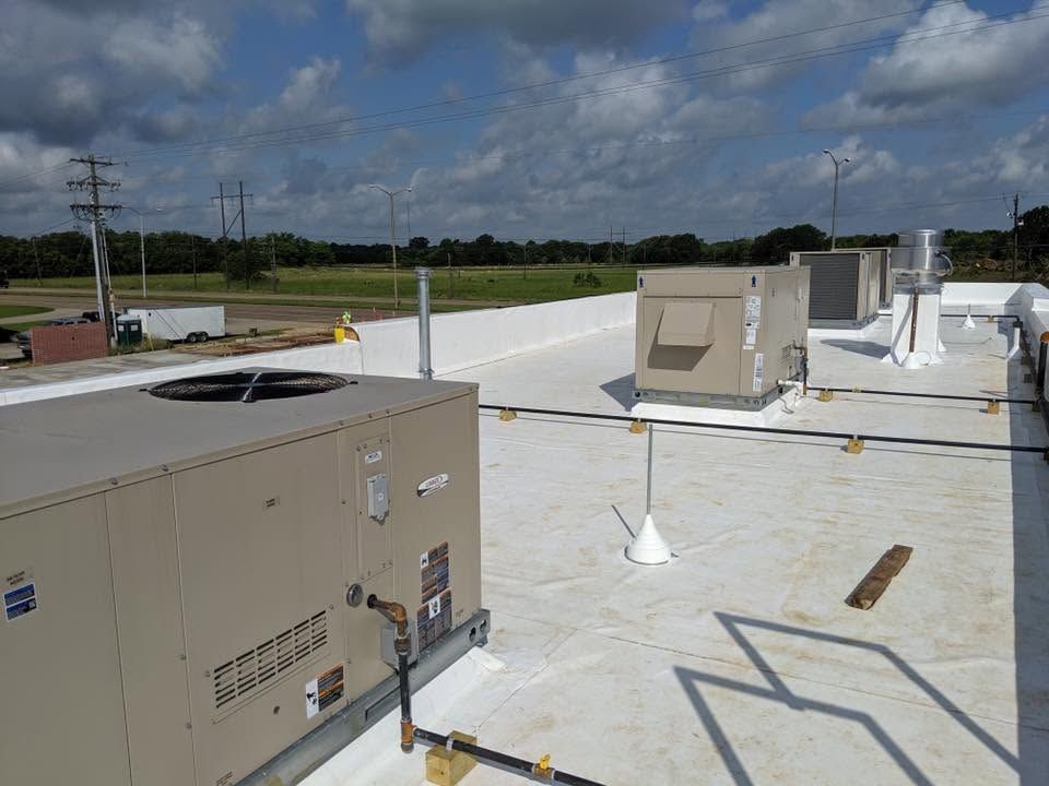 Rooftop HVAC units on a flat white commercial roof under a cloudy sky.