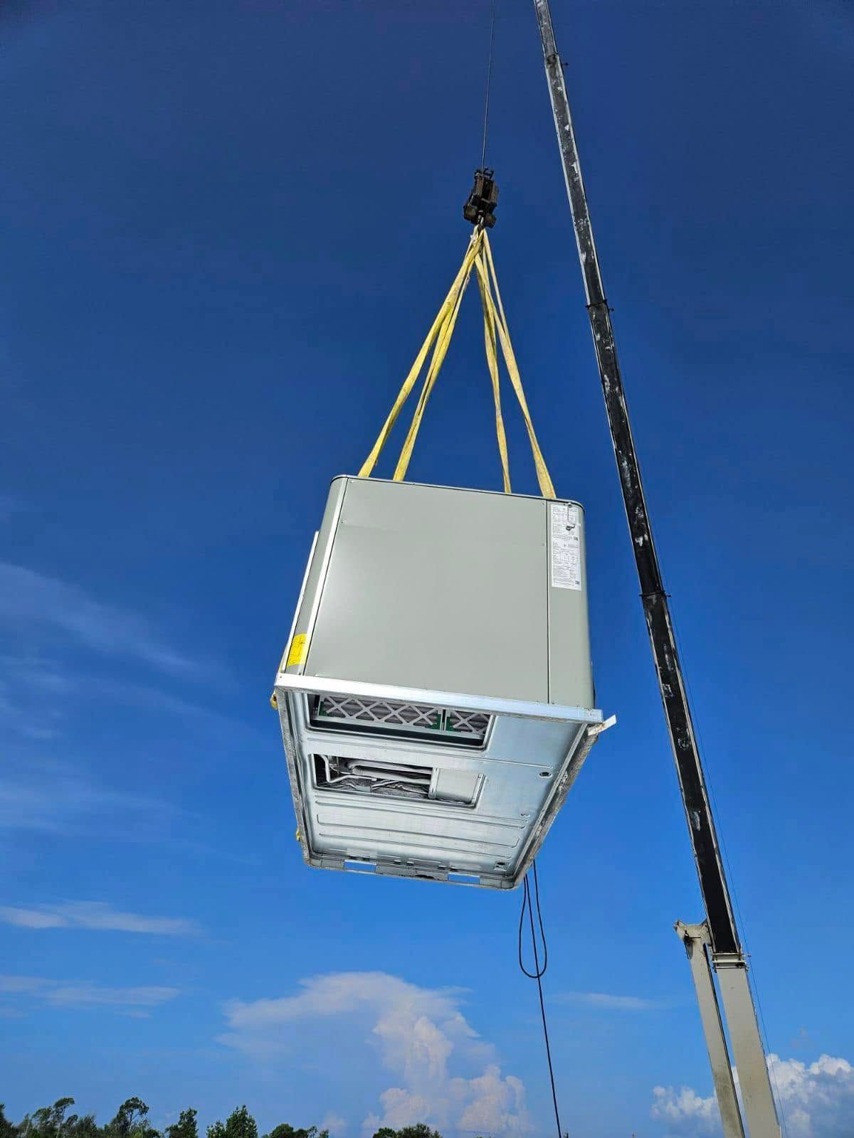 White appliance being lifted by crane against a blue sky