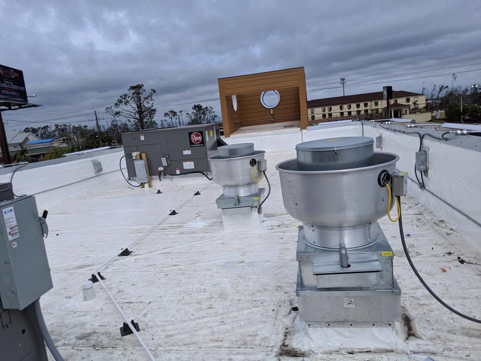 Rooftop HVAC units on a white roof under a cloudy sky, with a wooden sign in the background