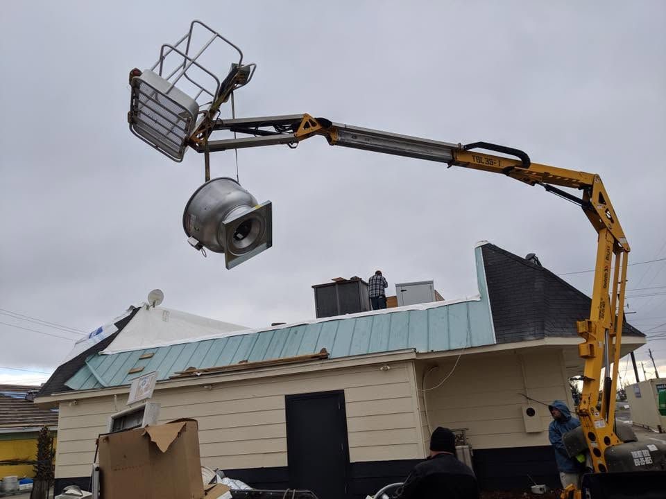 Bucket truck lifts large metal object over damaged roof under gray sky
