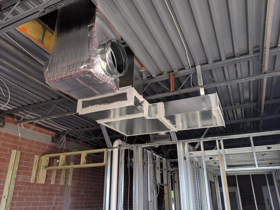 Exposed HVAC ductwork and ceiling framing in an unfinished interior space with metal studs and brick walls