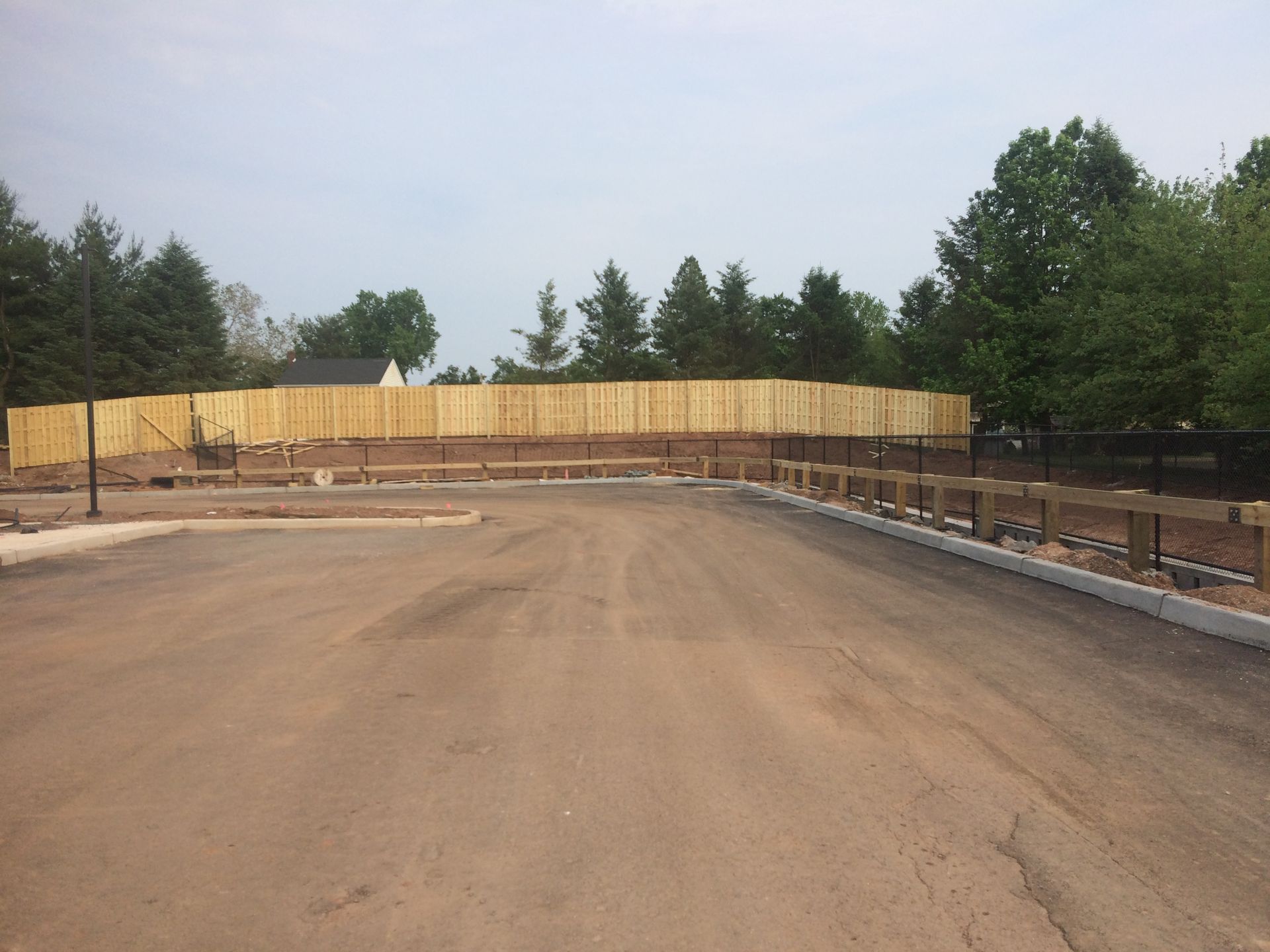 Paved road with wooden fence and trees in the background under a cloudy sky.