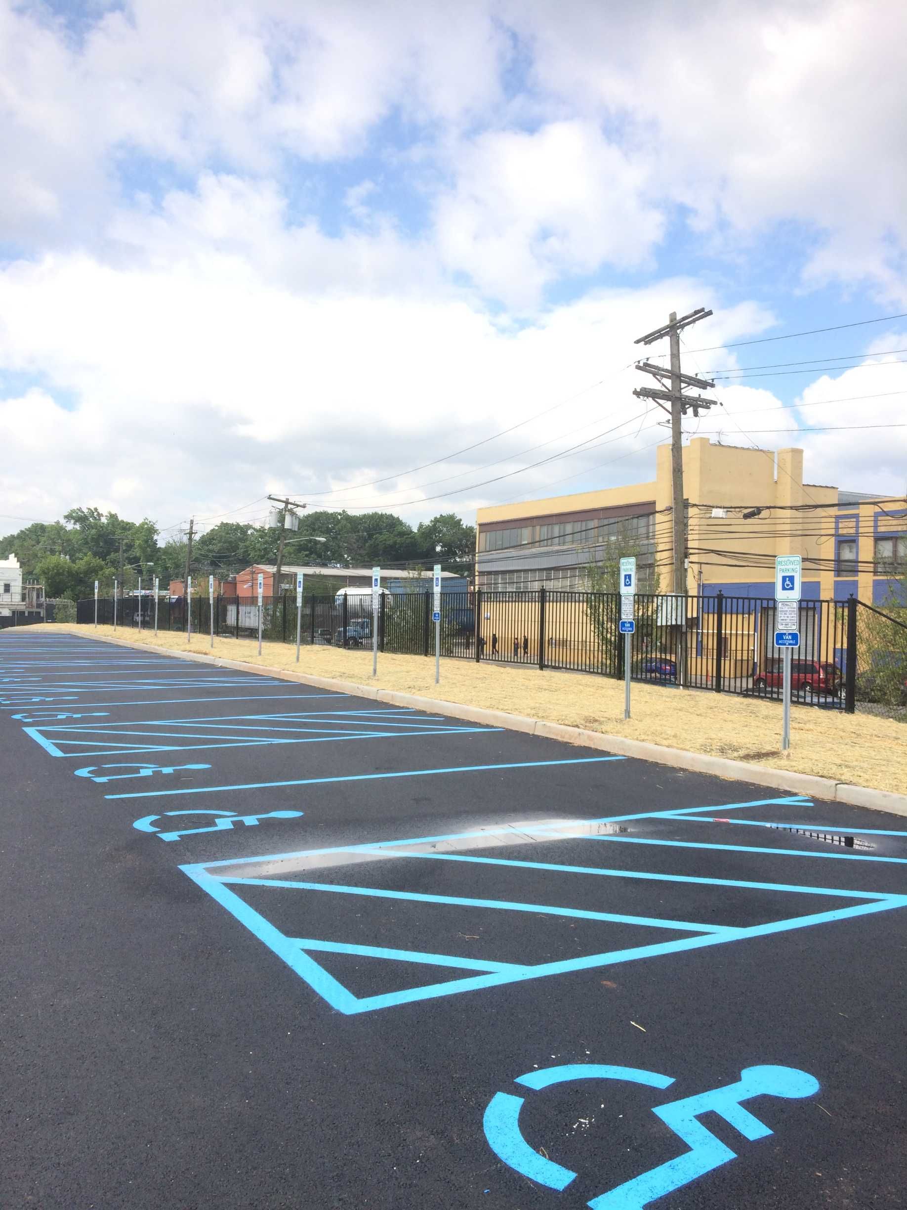 Parking lot with several blue-marked handicapped parking spaces, near a building and utility poles.