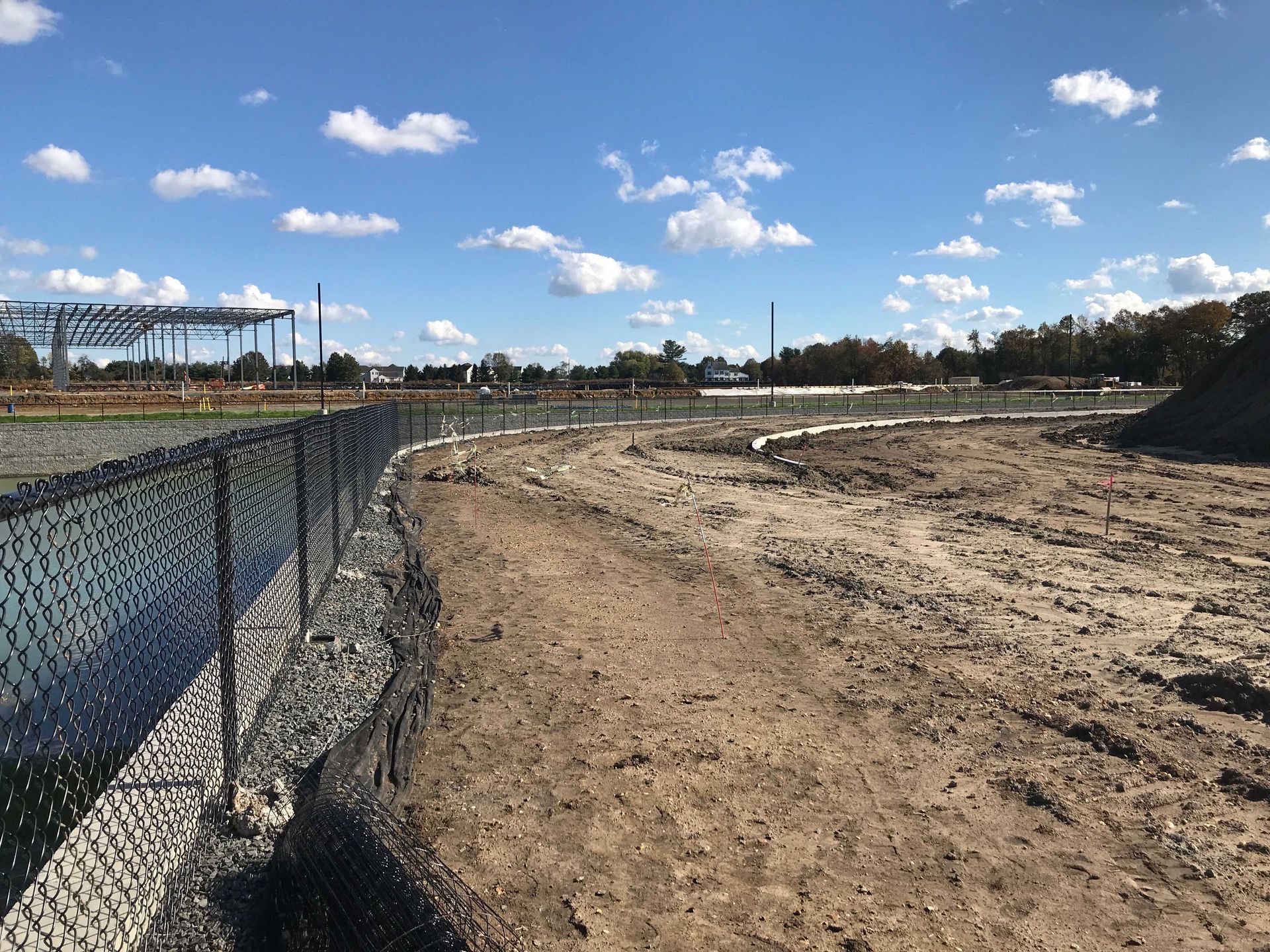 Construction site with dirt path, chain-link fence, and blue sky.
