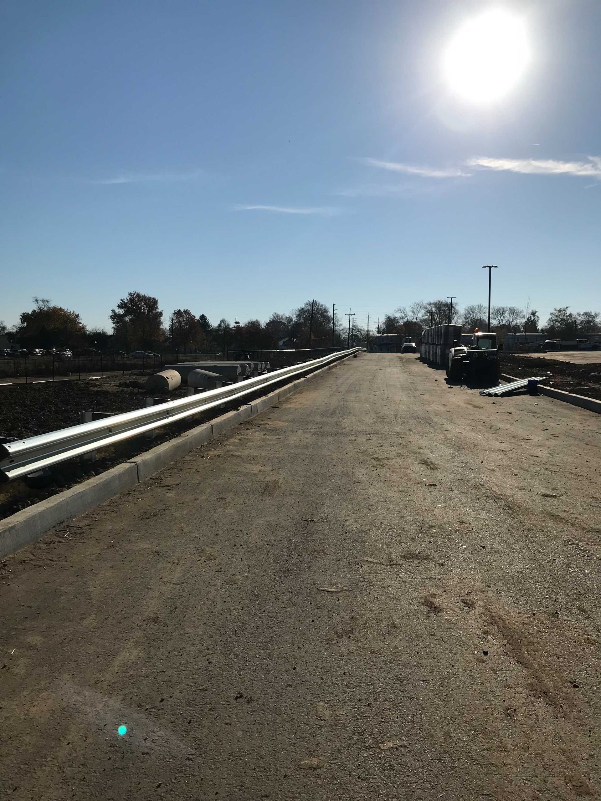 Gravel road with metal guardrail, bright sun in a clear sky. Construction site.