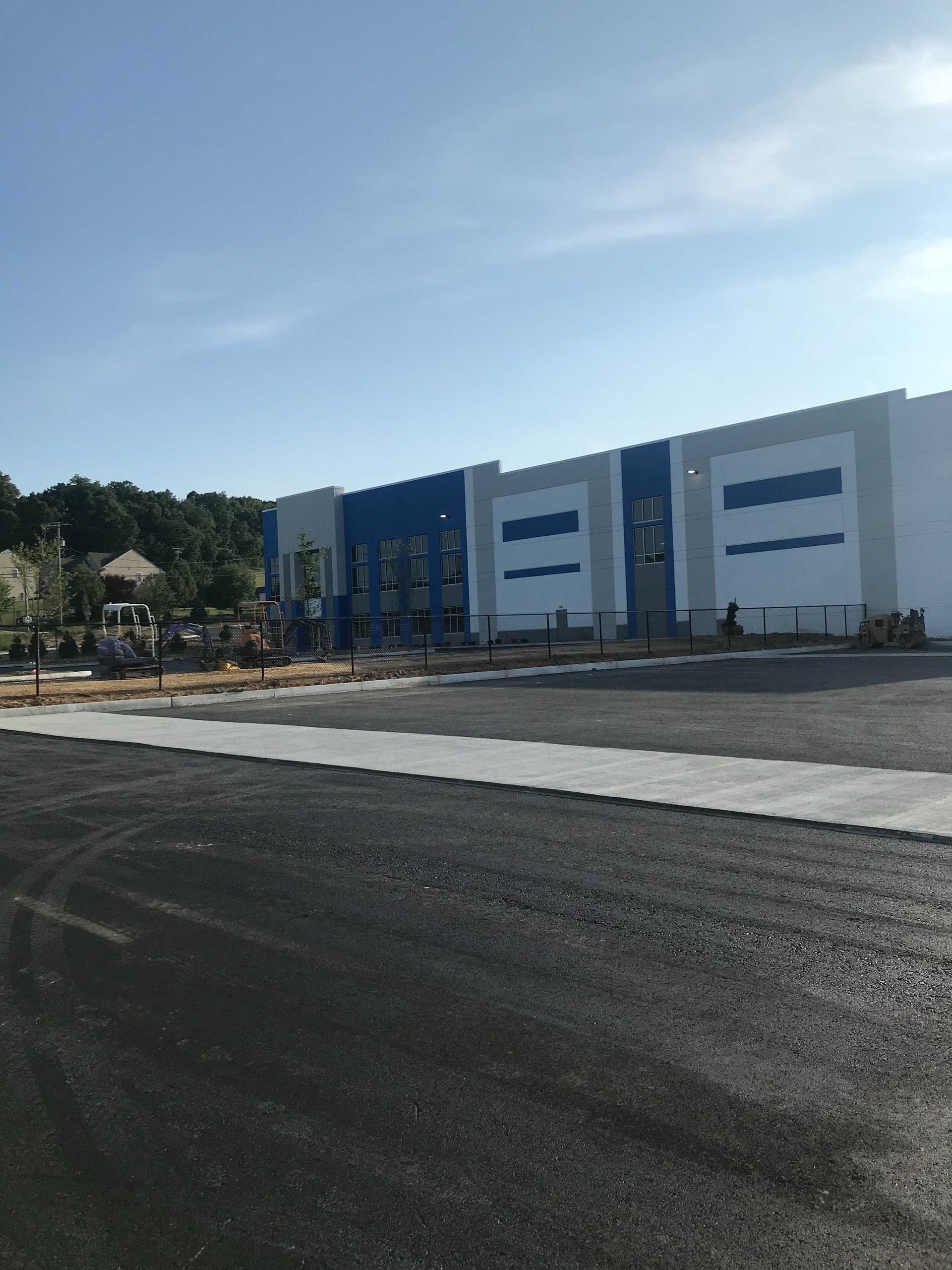 New commercial building under construction; blue and white exterior, asphalt in foreground, trees in background.