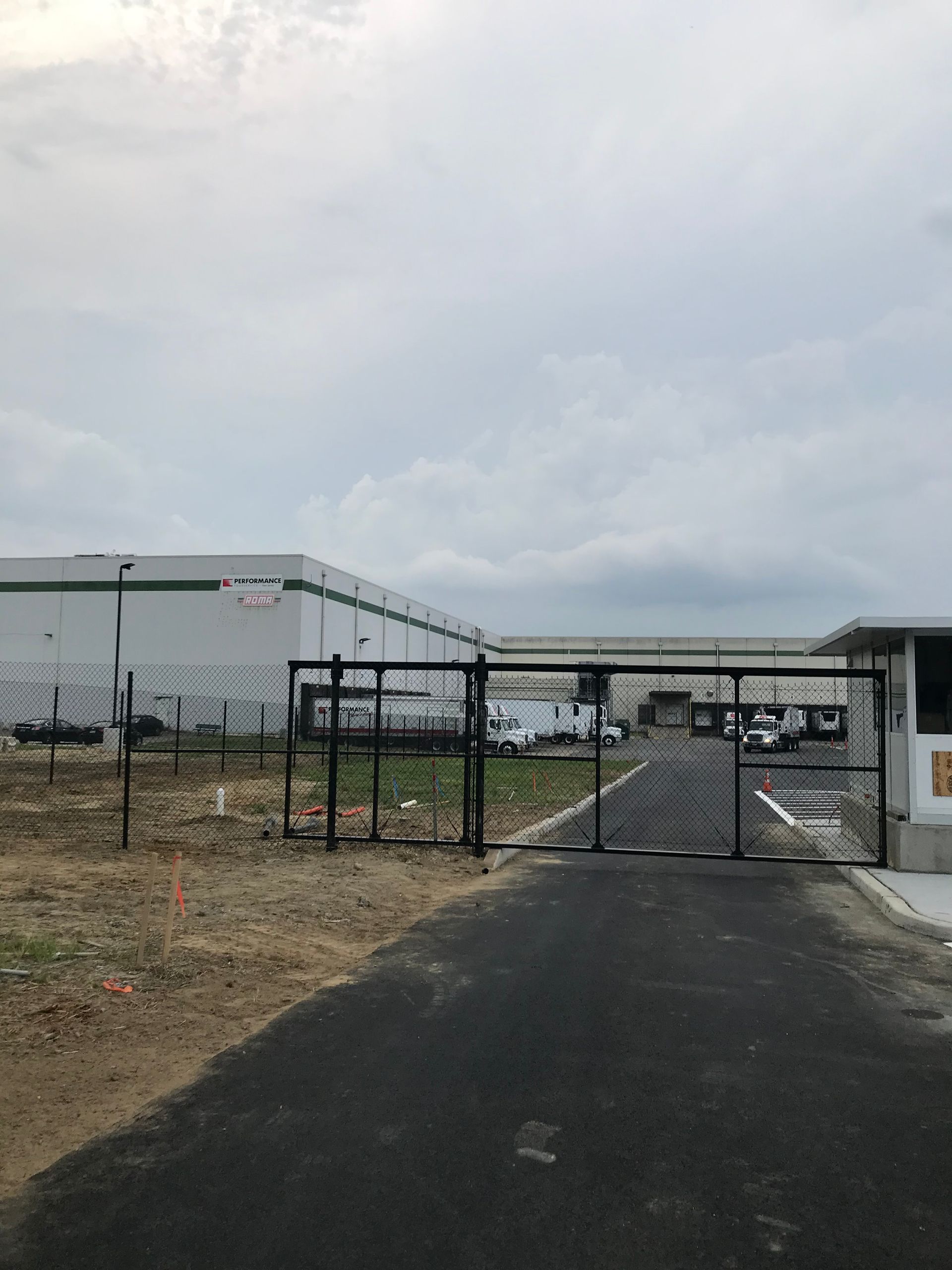 Black gate and security booth at a warehouse entrance on a cloudy day.