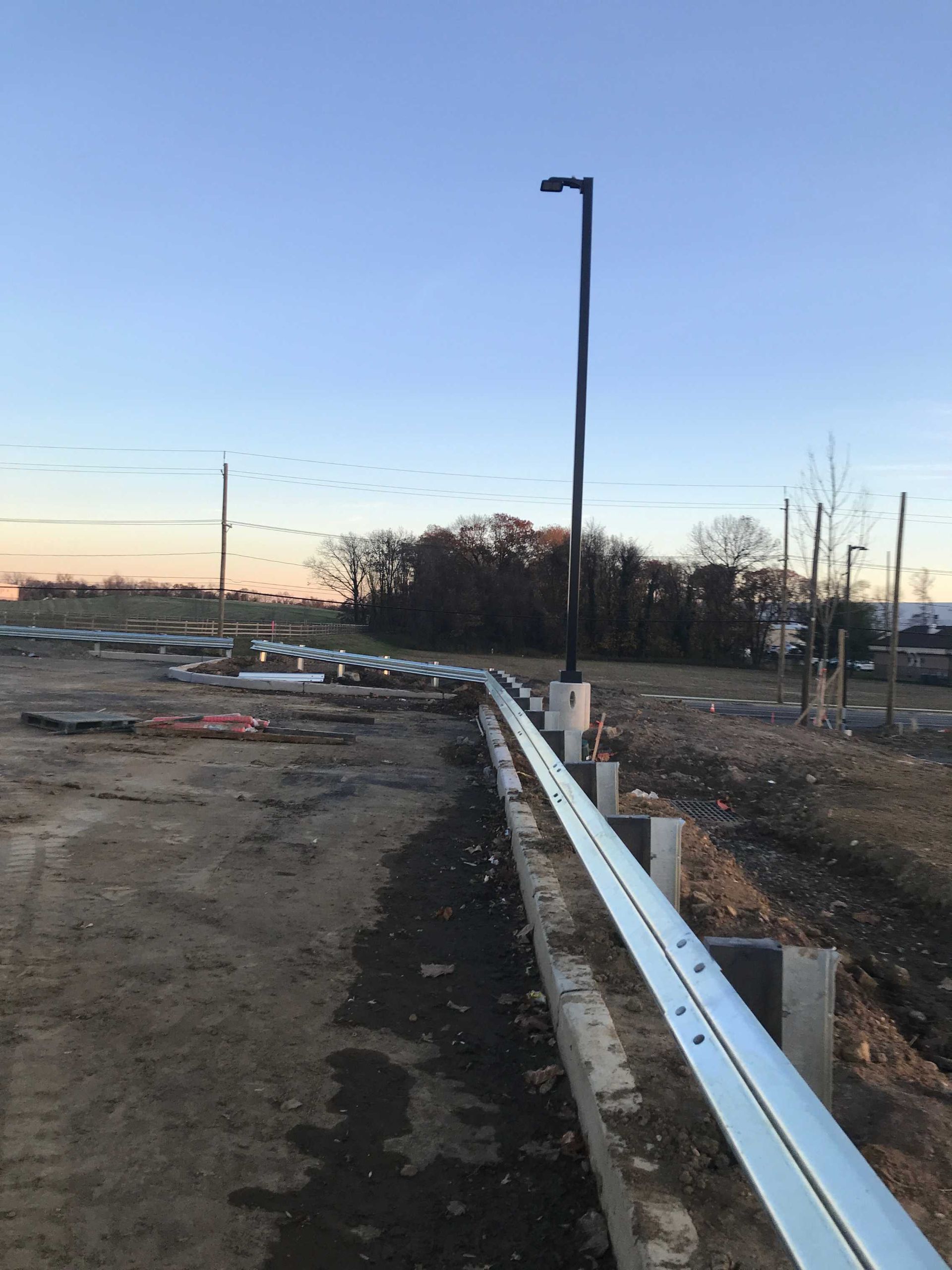 Construction site with a metal guardrail, light pole, and a dirt road.