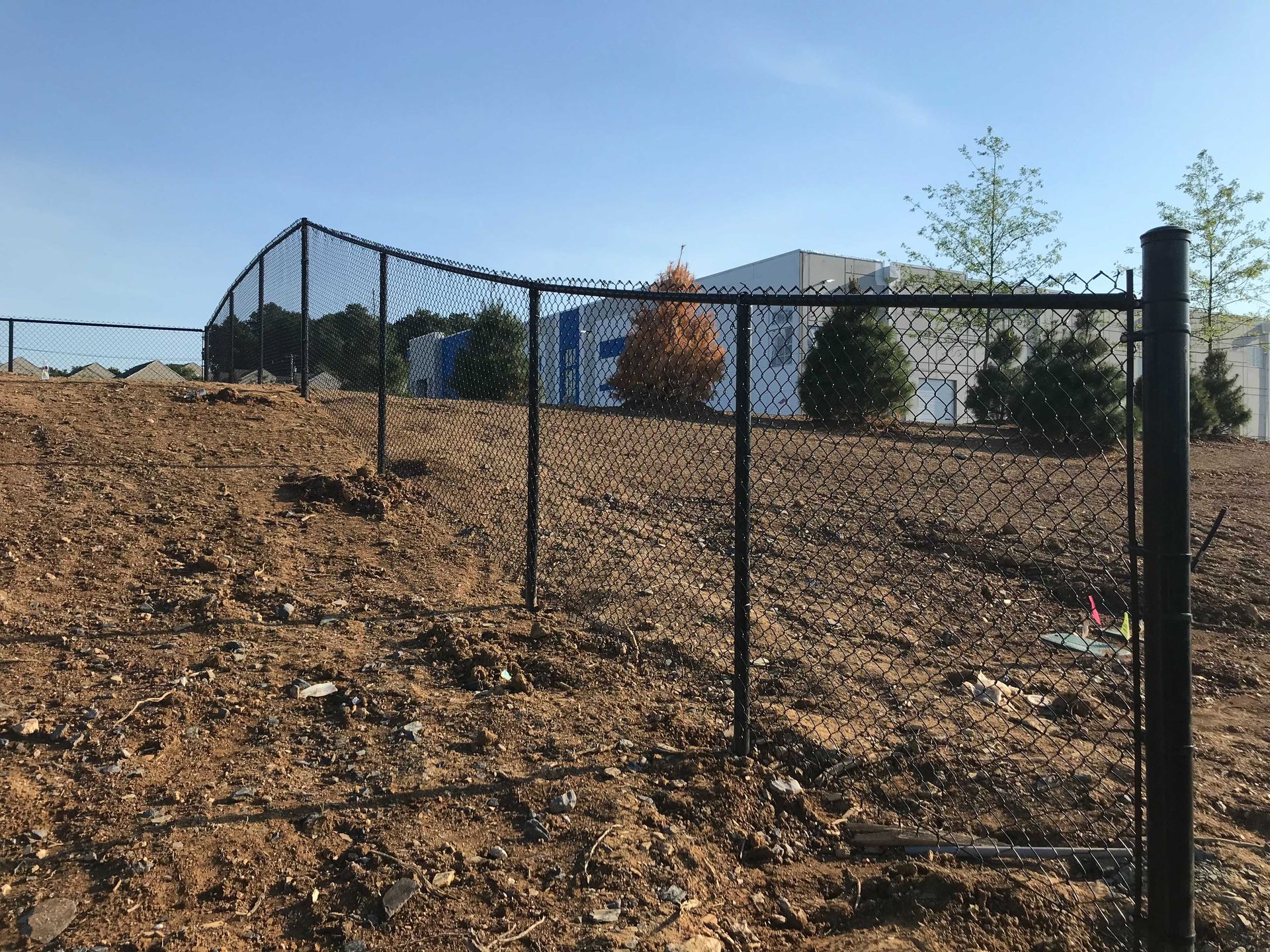 Black chain-link fence on a hill, brown soil, blue sky.