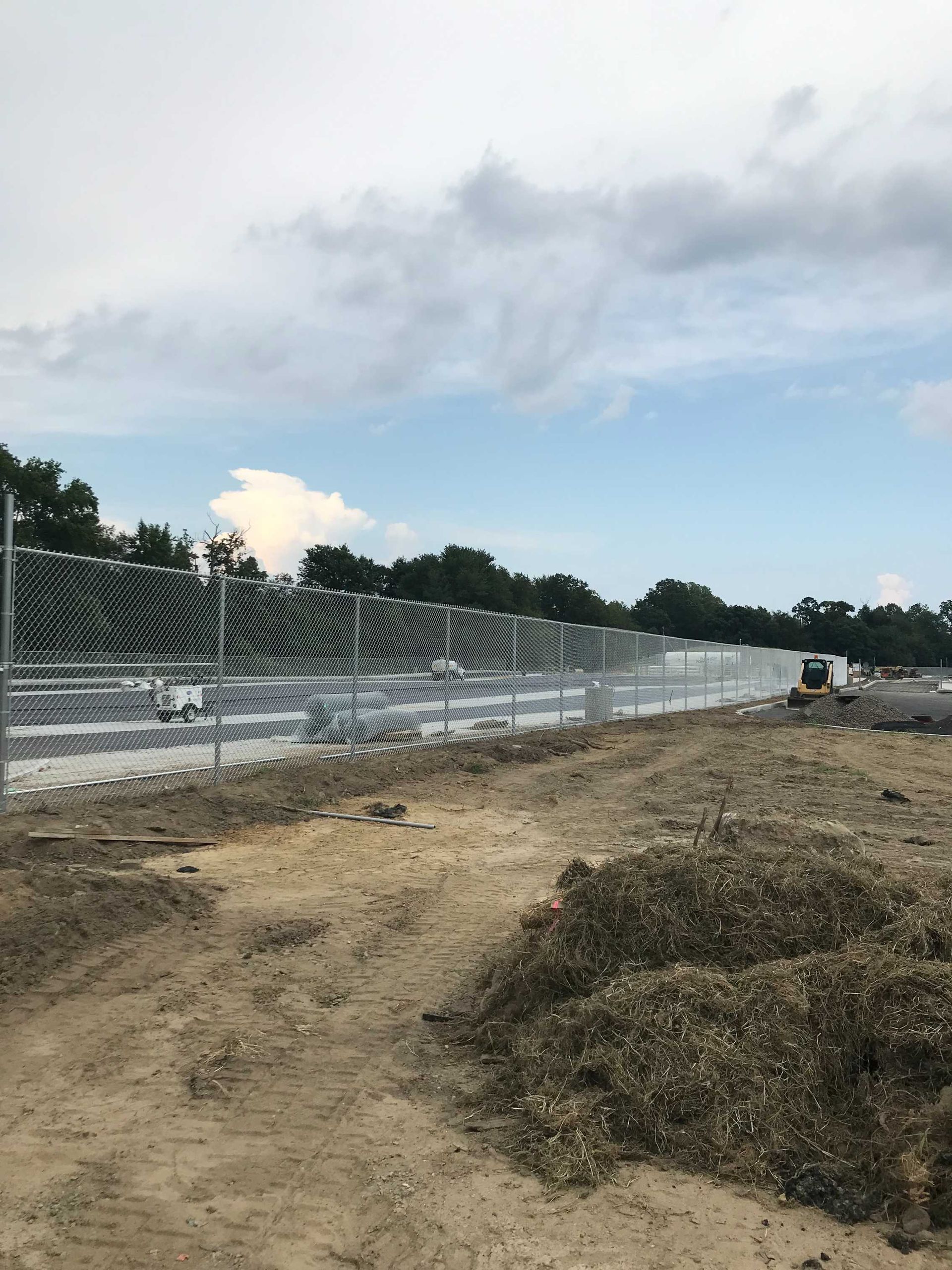 A silver metal fence along a dirt area with a partly cloudy sky in the background.
